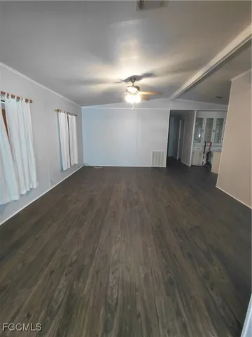 an empty room with wooden floor chandelier fan and windows