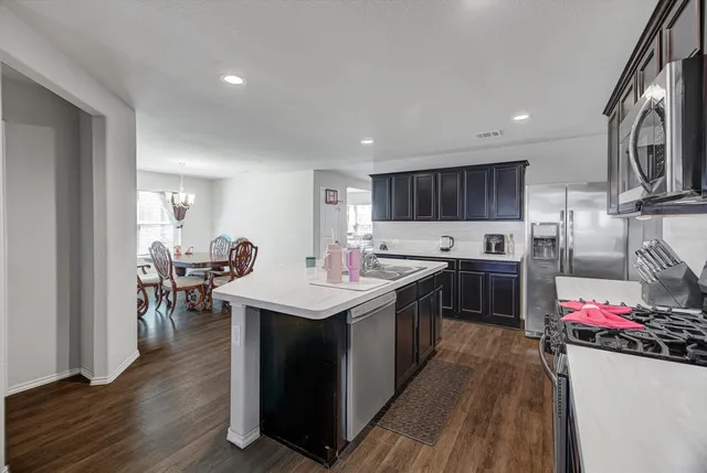 a kitchen with stainless steel appliances granite countertop a stove top oven a sink dishwasher and a refrigerator with wooden floor