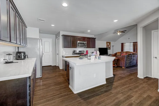 a kitchen with stainless steel appliances kitchen island granite countertop a stove top oven a sink a refrigerator and white cabinets with wooden floor