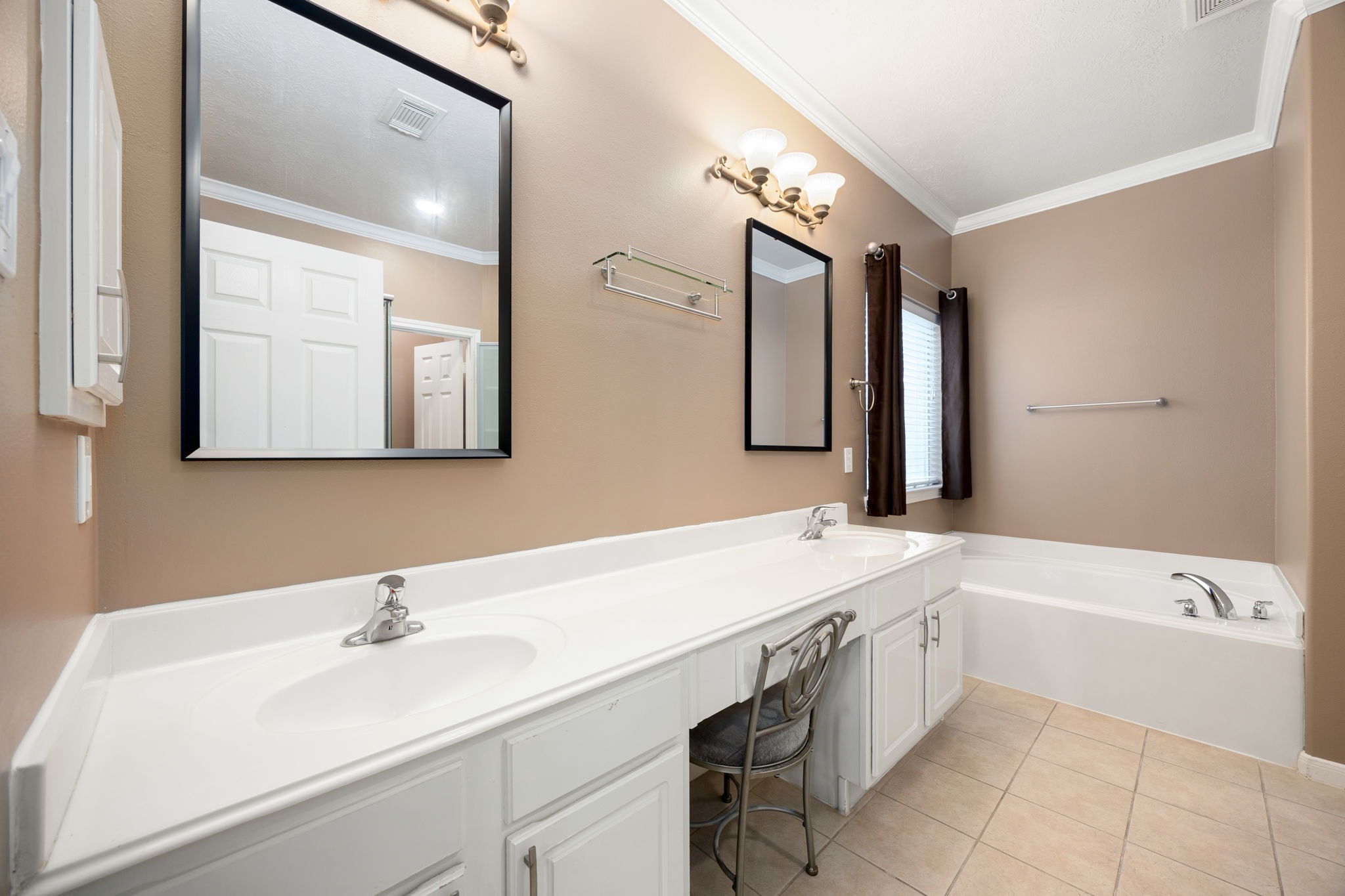 4526 Countrypines Drive Spring, TX 77388 - Photo 23 of 38 Primary bathroom oasis showcasing a long dual-sink vanity with abundant cabinet storage and modern framed mirrors. A deep soaking tub sits tucked under a window, offering a perfect spot to unwind at the end of the day.