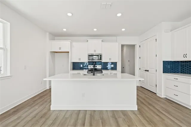 a large white kitchen with stainless steel appliances granite countertop a stove a sink a refrigerator and white cabinets with wooden floor