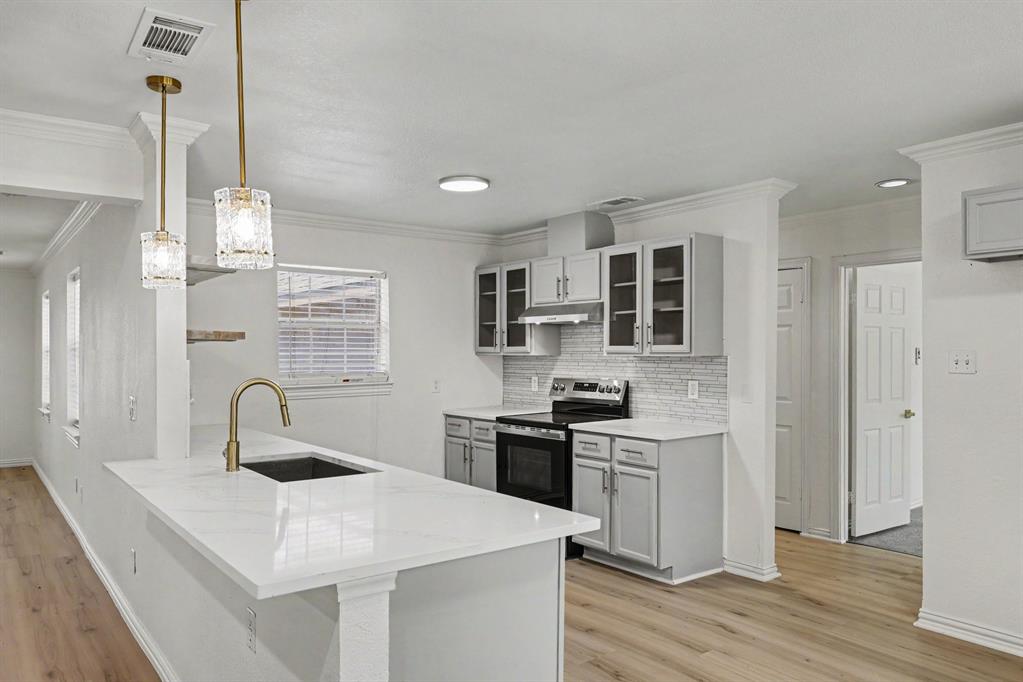 307 Dixon Street Terrell, TX 75160 - Photo 8 of 32 Kitchen featuring a large island with a gold-tone faucet and undermount sink, light gray cabinetry, glass-front upper cabinets, a tile backsplash, and wood-finish flooring