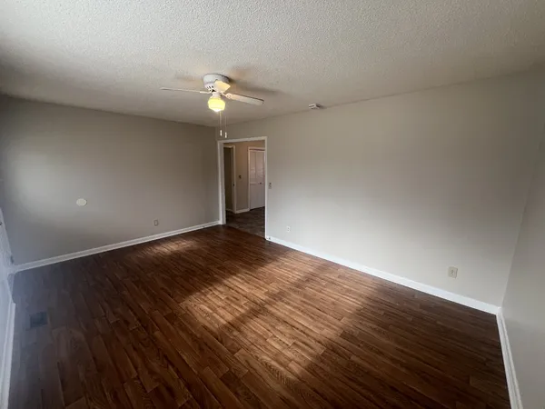 a view of an empty room with wooden floor and a ceiling fan