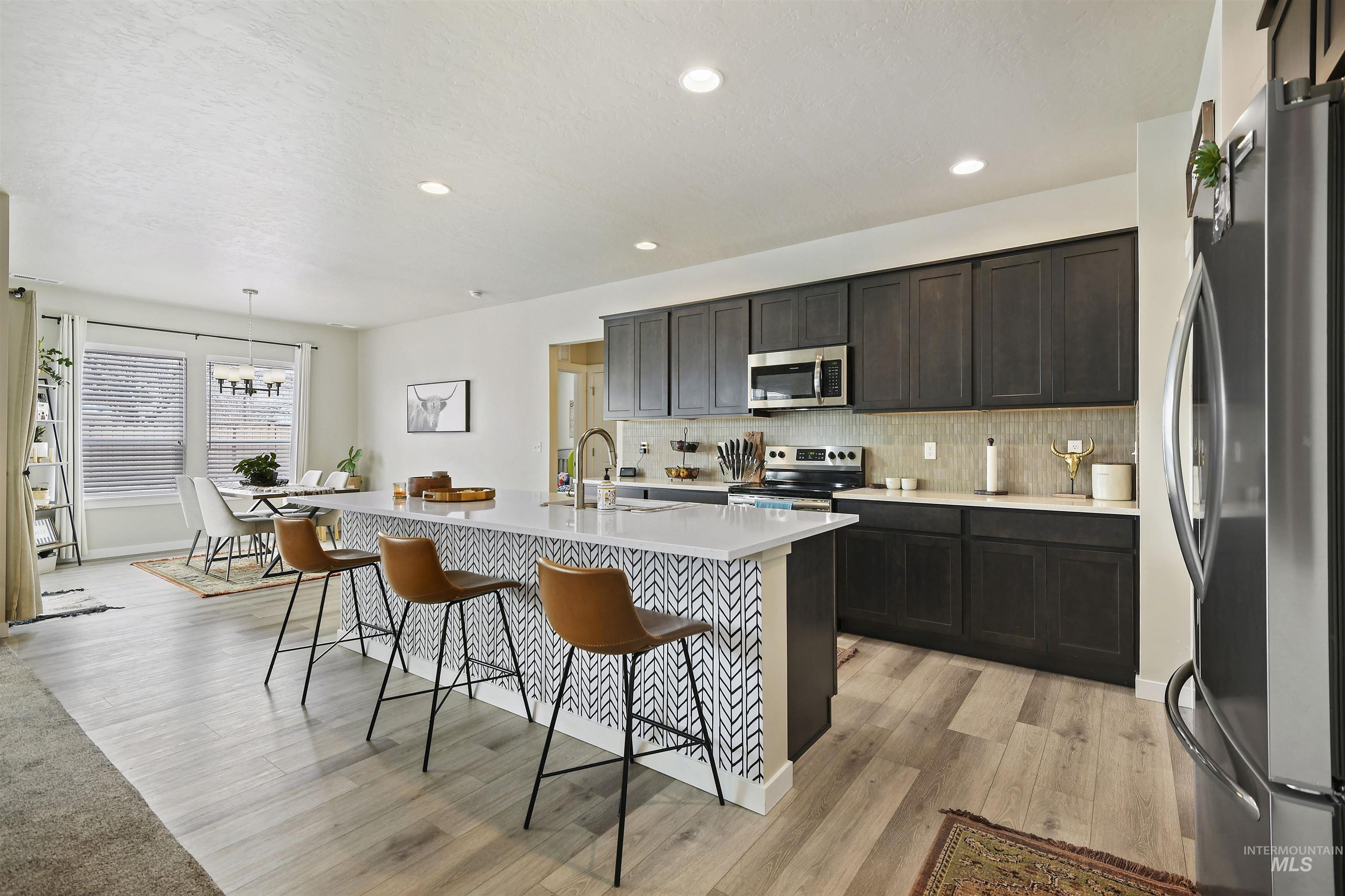 13472 Deodar Street Caldwell, ID 83607 - Photo 7 of 22 Kitchen with stainless steel appliances, tasteful backsplash, a center island with sink, decorative light fixtures, and a breakfast bar area