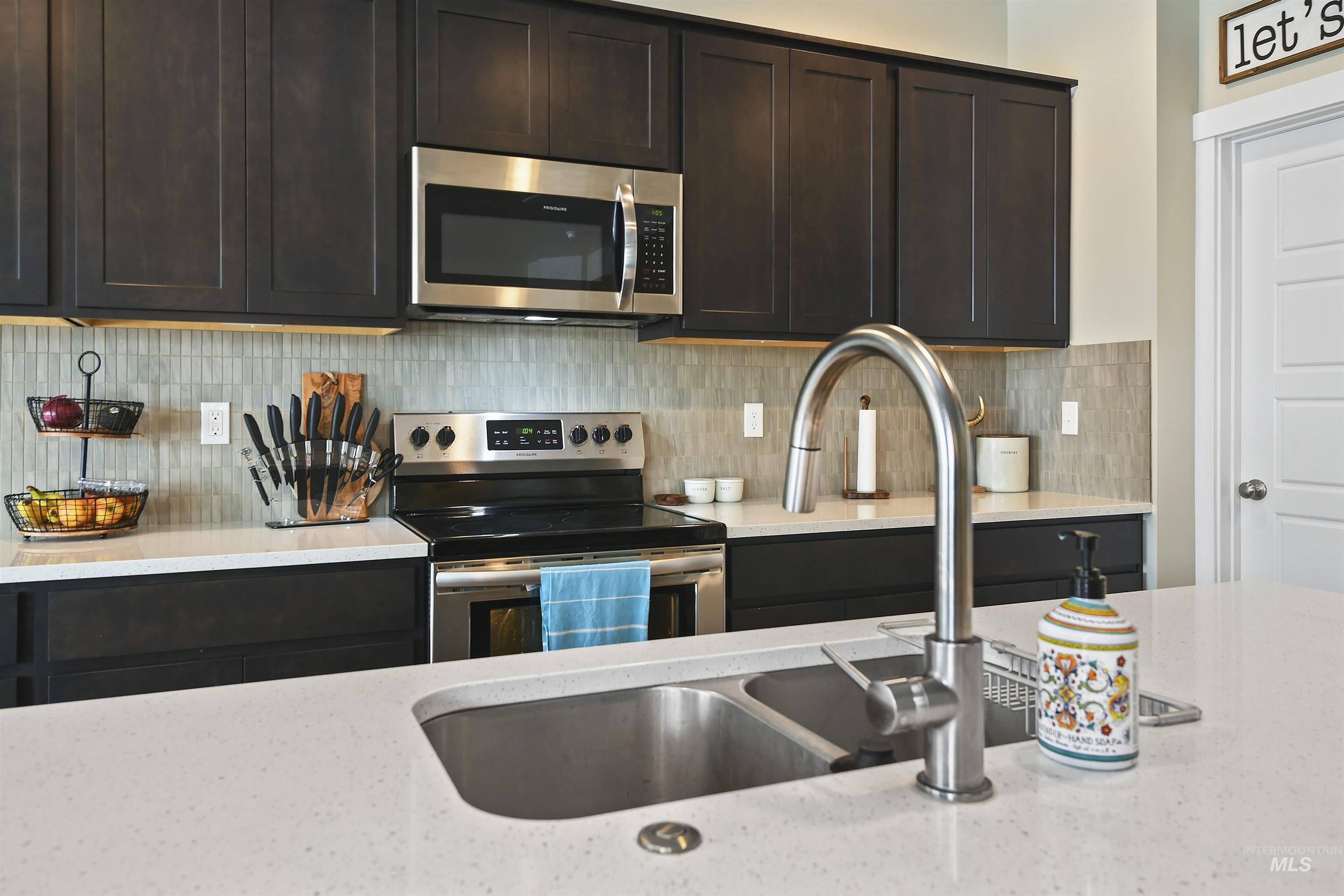 13472 Deodar Street Caldwell, ID 83607 - Photo 8 of 22 Kitchen featuring appliances with stainless steel finishes, light stone countertops, dark brown cabinets, and backsplash