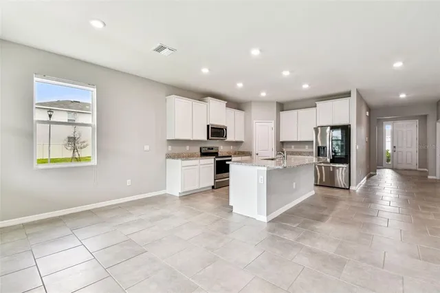 a large kitchen with kitchen island a sink a stove a refrigerator and white cabinets with wooden floor