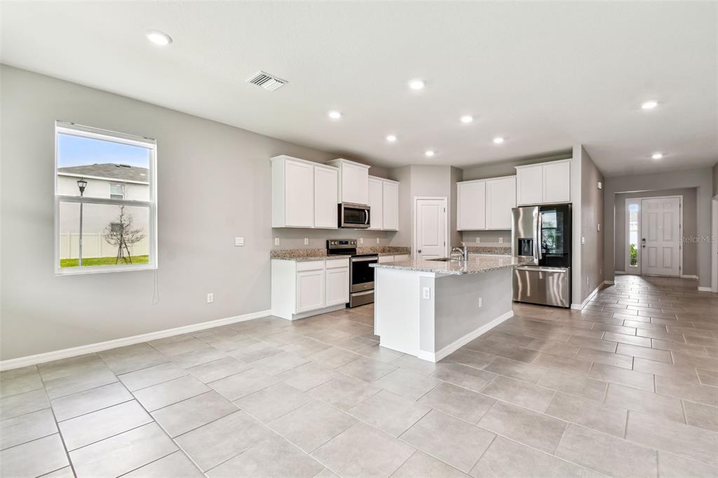 33870 Field Maple Loop Wesley Chapel, FL 33545 - Photo 1 of 38 a large kitchen with kitchen island a sink a stove a refrigerator and white cabinets with wooden floor