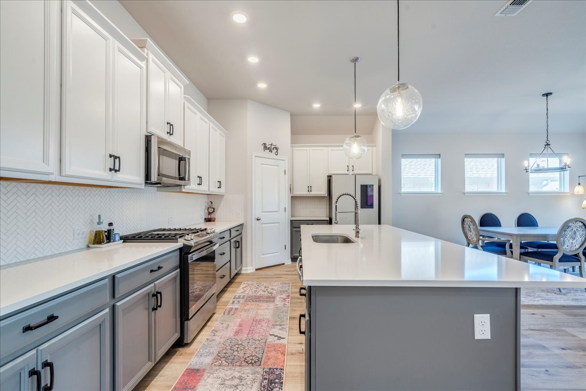 200 Christi Court Kyle, TX 78640 - Photo 13 of 40 Kitchen featuring gray cabinetry, appliances with stainless steel finishes, white cabinets, decorative light fixtures, and tasteful backsplash