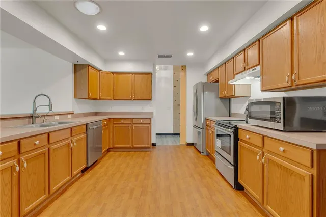 a kitchen with stainless steel appliances granite countertop a sink a stove top oven a refrigerator with wooden cabinets and floor