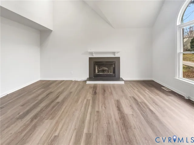 an empty room with wooden floor a fireplace and windows