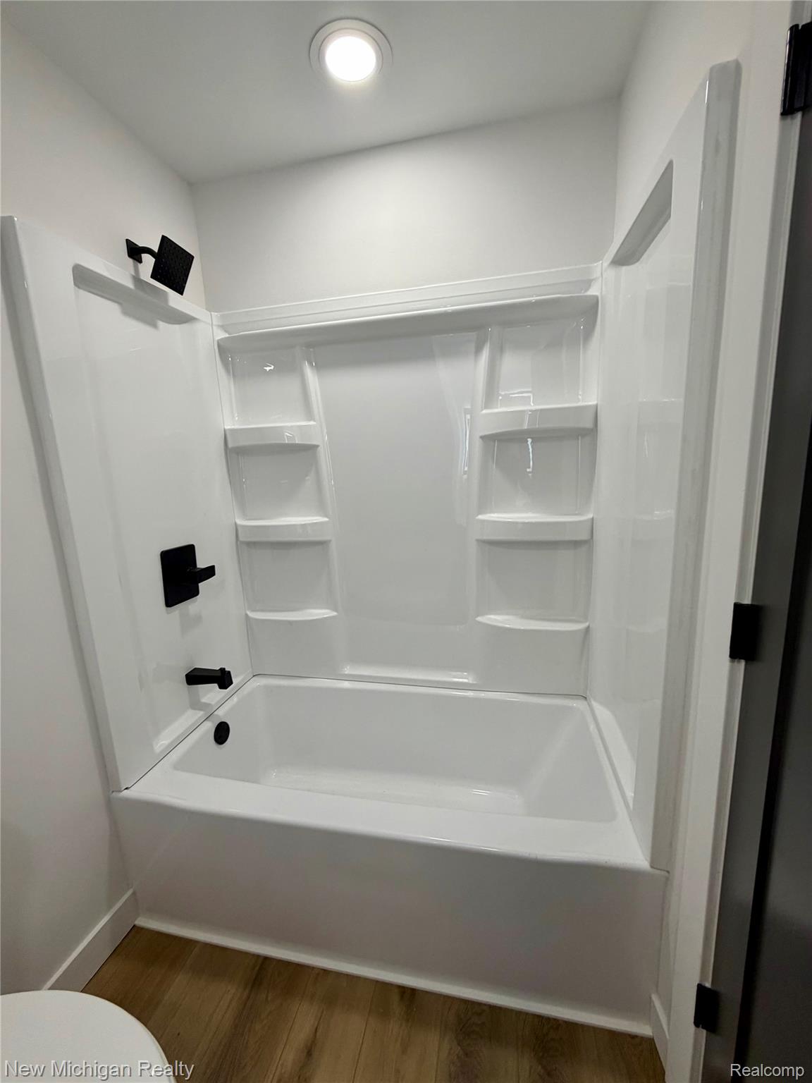 7104 Willard Road Millington, MI 48746 - Photo 15 of 30 Full bathtub with integrated white surround, featuring matte black fixtures, recessed ceiling lighting, and wood-finish flooring