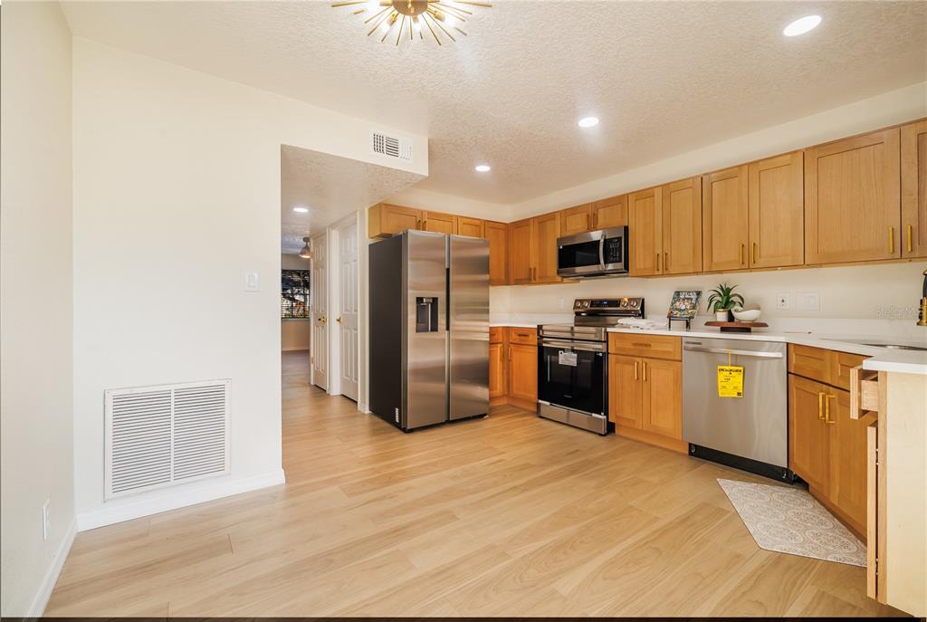 6922 Woodlake Drive, Unit 103 Orlando, FL 32810 - Photo 5 of 16 a kitchen with granite countertop a refrigerator oven a sink dishwasher and white cabinets with wooden floor