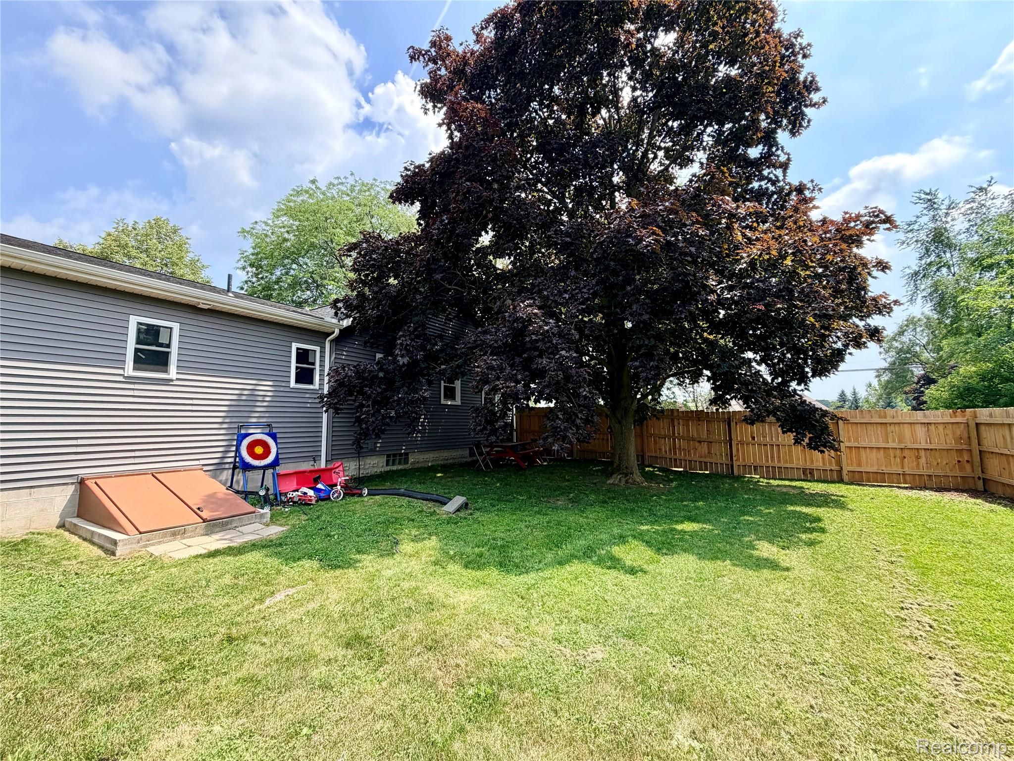 3840 East Dunbar Road Monroe, MI 48161 - Photo 3 of 38 Expansive rear yard featuring a privacy fence, mature shade tree, and a basement entry