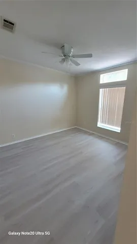 an empty room with wooden floor ceiling fan and windows