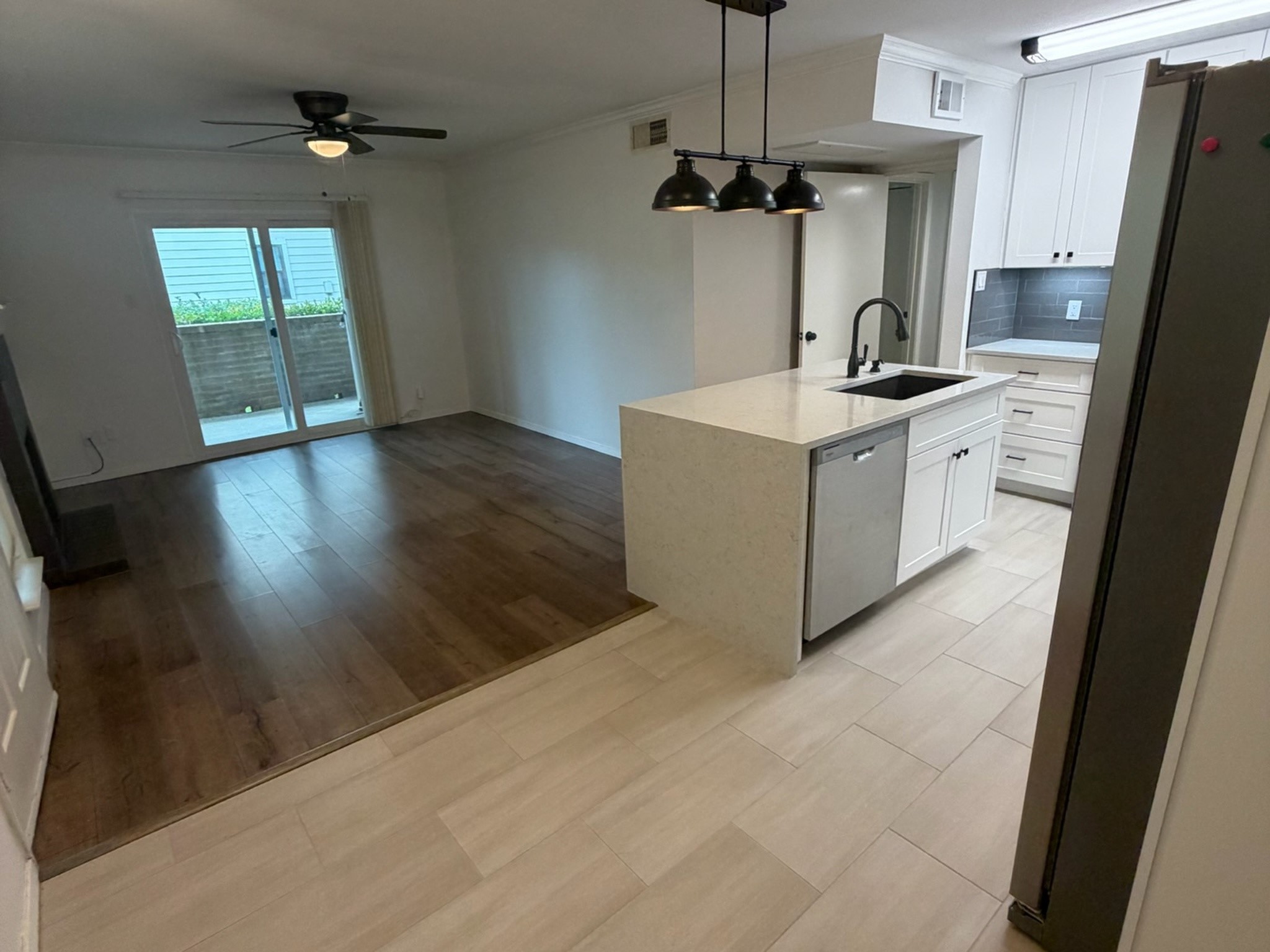 3500 Tangle Brush Drive, Unit 65 Spring, TX 77381 - Photo 5 of 20 Open-concept layout connects the updated kitchen and living area, featuring contrasting flooring, a waterfall-edge island with sink and dishwasher, modern pendant lighting, and sliding glass doors that extend the living space to the private patio.