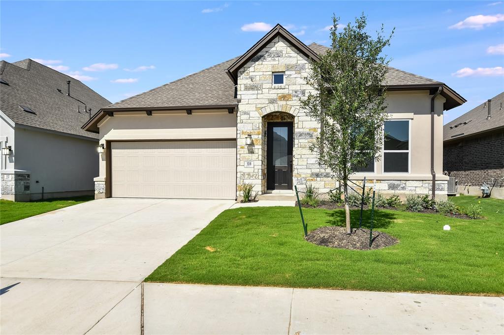 French country home featuring stone siding, roof with shingles, an attached garage, driveway, and a front yard