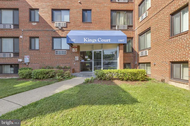 a view of a brick house with a yard plants and large tree