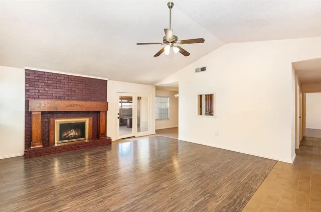 a view of an empty room with wooden floor fireplace and a window