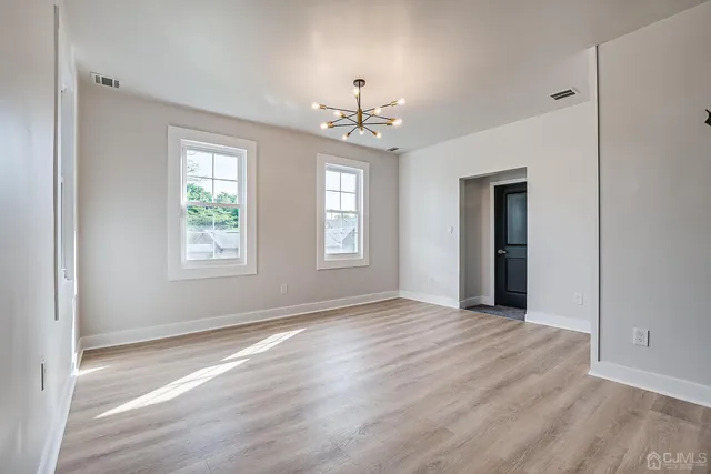 an empty room with wooden floor chandelier and windows