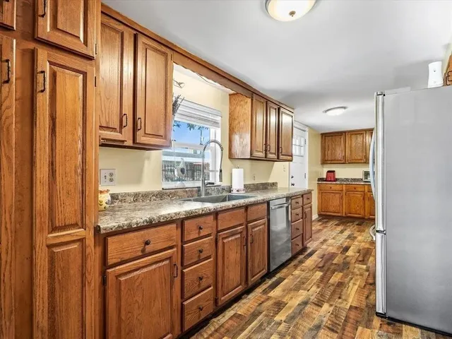 a kitchen with stainless steel appliances granite countertop a refrigerator a sink dishwasher a stove and white countertops with wooden floor