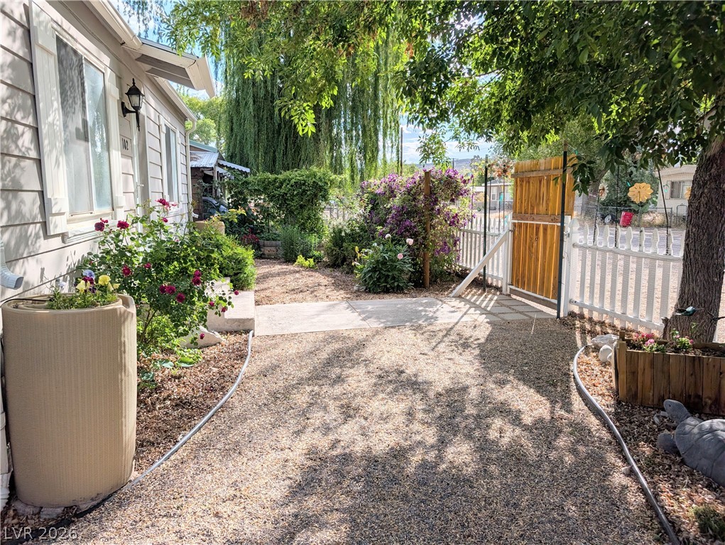 102 Rowan Drive Caliente, NV 89008 - Photo 2 of 28 A welcoming front yard with gravel path and vibrant rose bushes leads to a charming picket fence.