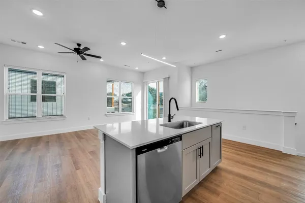 a kitchen with a sink dishwasher and white cabinets with wooden floor