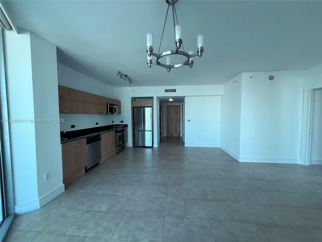 a view of an empty room with kitchen and a window