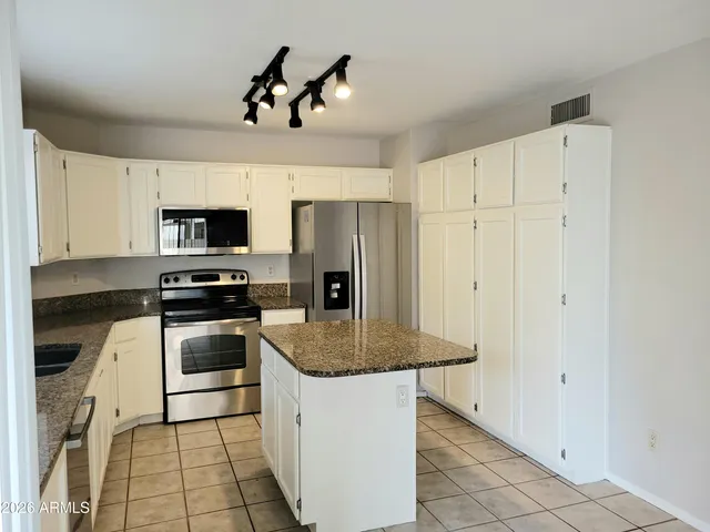 a kitchen with stainless steel appliances granite countertop a sink a stove a refrigerator cabinets and a dining table