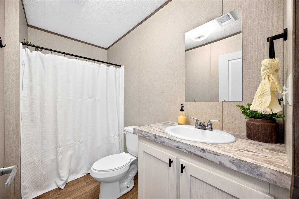 3208 Northeast County Road Powell, TX 75153 - Photo 18 of 29 Bathroom featuring a shower with a privacy curtain, a toilet, a vanity with an integrated sink, a wall-mounted mirror, and wood-finish flooring