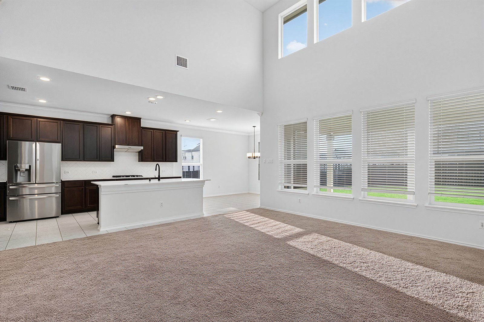 4600 Ercolano Lane Round Rock, TX 78665 - Photo 14 of 37 Open-concept living space featuring high ceilings, light brown carpet, and a kitchen with dark wood-finish cabinetry, a white island, and stainless steel appliances