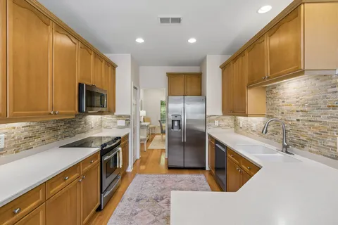 a kitchen with stainless steel appliances granite countertop a sink a microwave a refrigerator and white cabinets with wooden floor