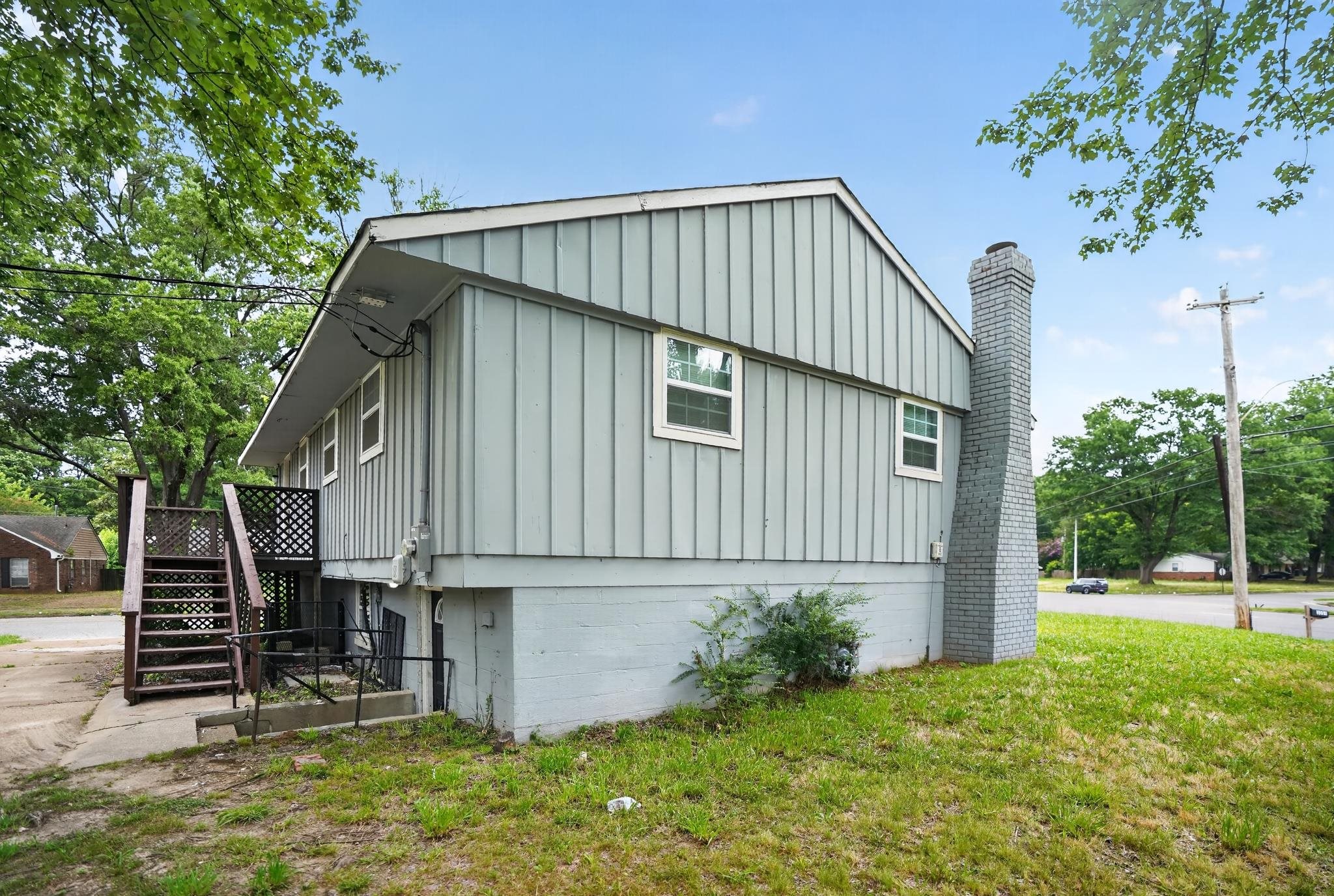 3391 South Perkins Road Memphis, TN 38118 - Photo 15 of 16 Light blue vertical siding exterior with white window trim, a gray brick chimney, and an exterior wood staircase with latticework detail
