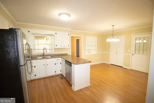 a kitchen with granite countertop a refrigerator a sink dishwasher stove and white cabinets with wooden floor