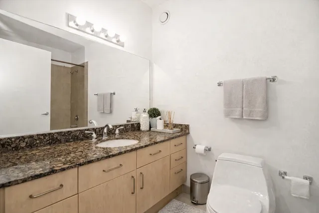 a bathroom with a granite countertop sink a large mirror and toilet