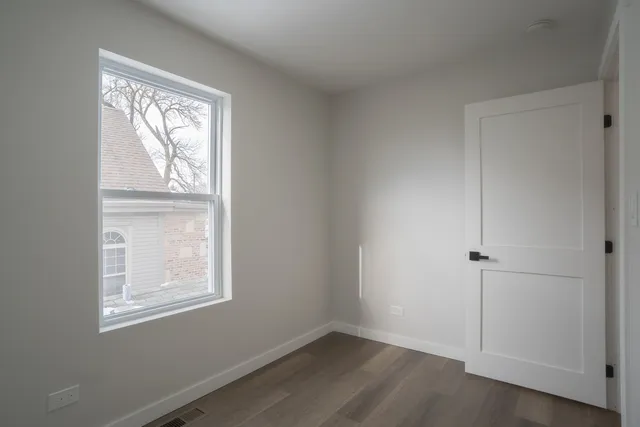 an empty room with wooden floor closet and windows