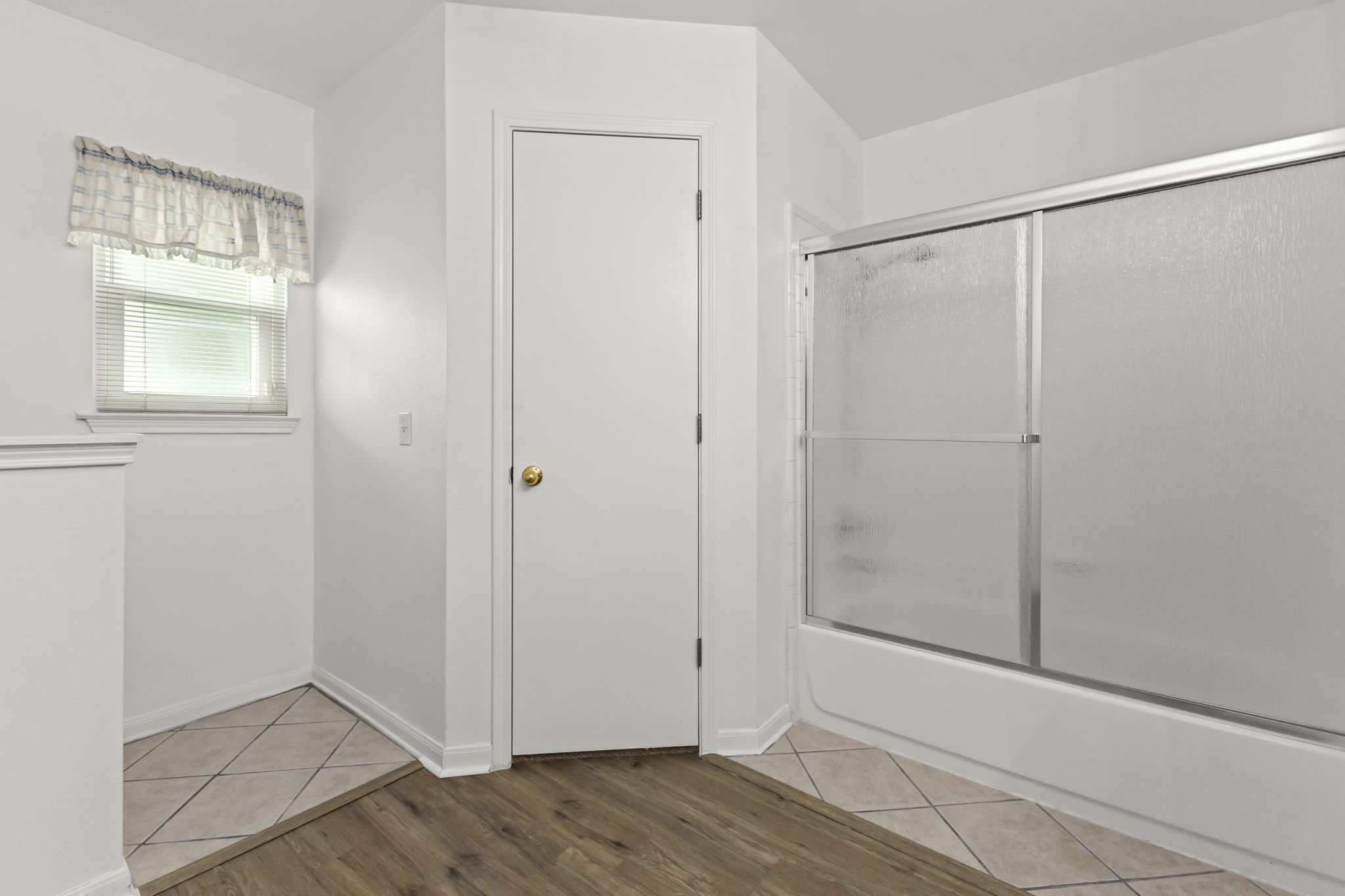 290 Bailey Loop Kyle, TX 78640 - Photo 22 of 33 Bathroom featuring a tub/shower combination with sliding glass doors, a window with blinds, a white door with a brass knob, and a blend of tile and wood-finish flooring