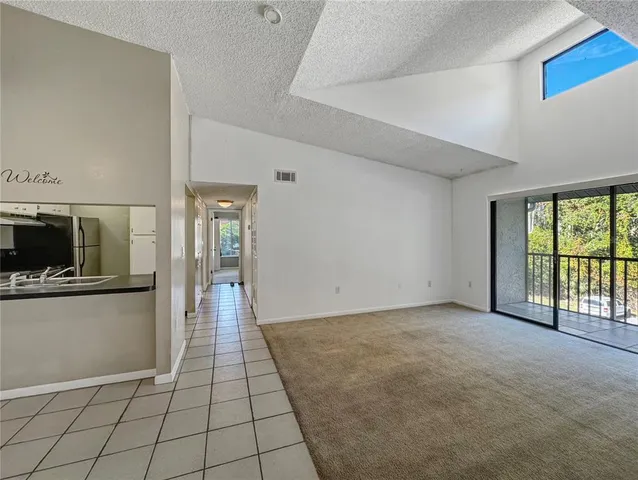 a view of an empty room with window and kitchen view