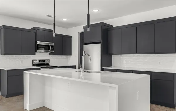 a kitchen with stainless steel appliances a sink a stove a microwave a refrigerator a center island and cabinets