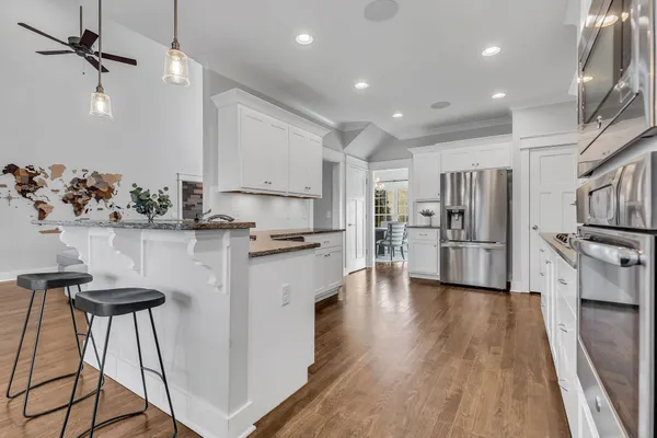 a kitchen with stainless steel appliances kitchen island granite countertop a refrigerator a stove and white cabinets with wooden floor