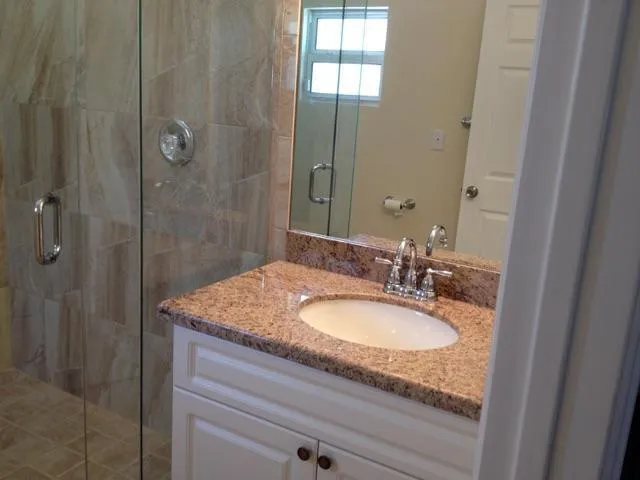 a bathroom with a granite countertop sink a mirror and shower