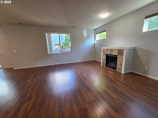 an empty room with wooden floor fireplace and windows
