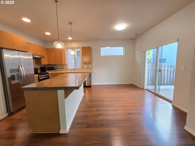 a kitchen with stainless steel appliances granite countertop a refrigerator a sink dishwasher a oven and a large island with wooden floor