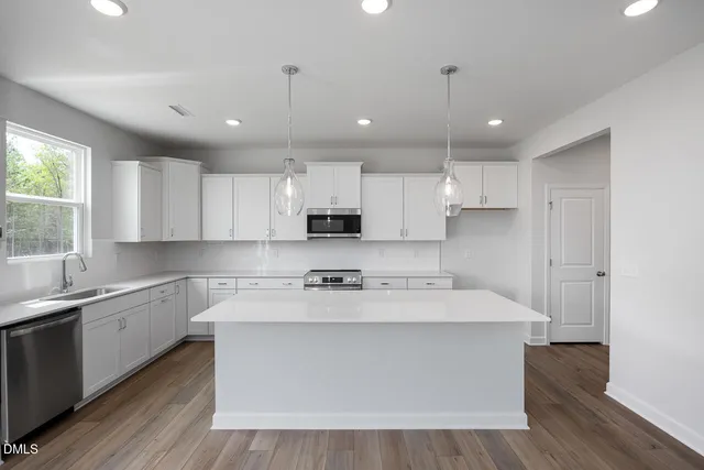 a large white kitchen with kitchen island a sink a center island stainless steel appliances and a window