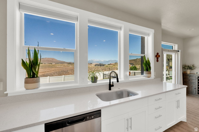 1857 Thunder Gulch Road Eagle Mountain, UT 84005 - Photo 13 of 50 Kitchen featuring white cabinetry, light-toned countertops, a stainless steel undermount sink with a black faucet, and a stainless steel dishwasher