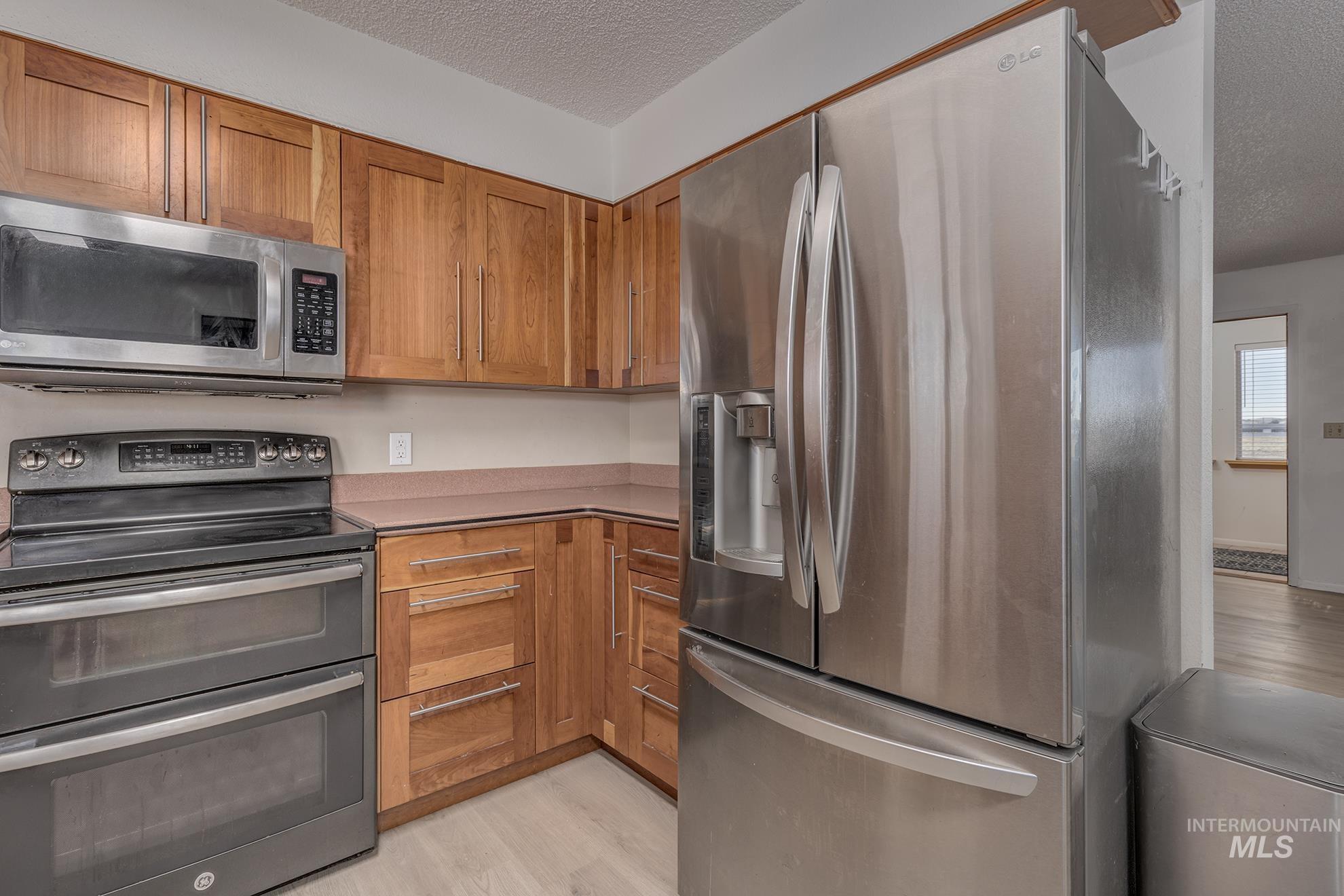 710 North 5th Street Nyssa, OR 97913 - Photo 12 of 36 Kitchen featuring appliances with stainless steel finishes, a textured ceiling, brown cabinetry, light wood-style flooring, and light countertops