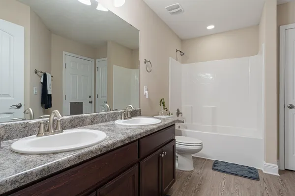 a bathroom with a granite countertop sink a toilet a mirror a vanity and shower
