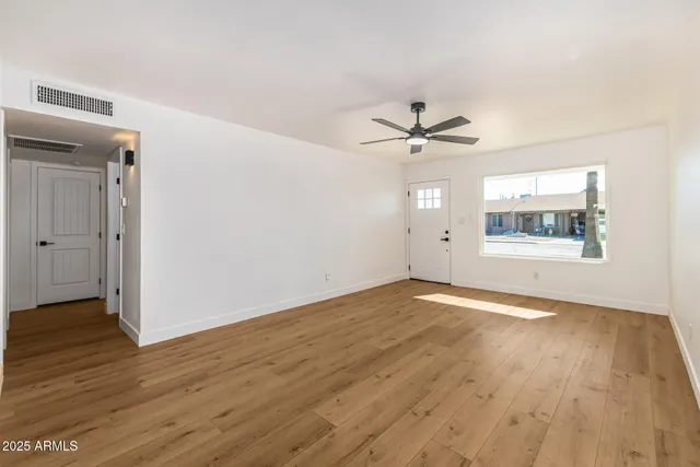 an empty room with wooden floor ceiling fan and windows