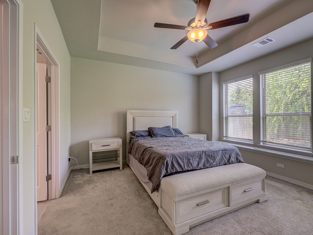 229 Heartleaf Road San Marcos, TX 78666 - Photo 25 of 40 A well-lit bedroom featuring a tray ceiling, ceiling fan, and carpeted floors, creating a comfortable and inviting atmosphere.