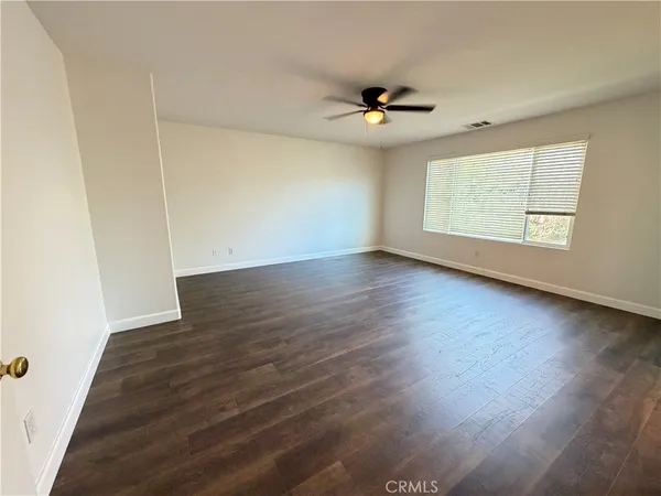 an empty room with wooden floor fan and windows