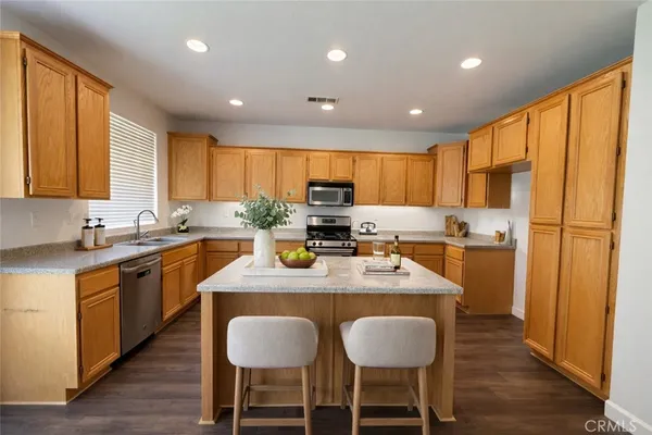 a kitchen with stainless steel appliances granite countertop wooden floor a refrigerator a sink a stove a dining table and chairs